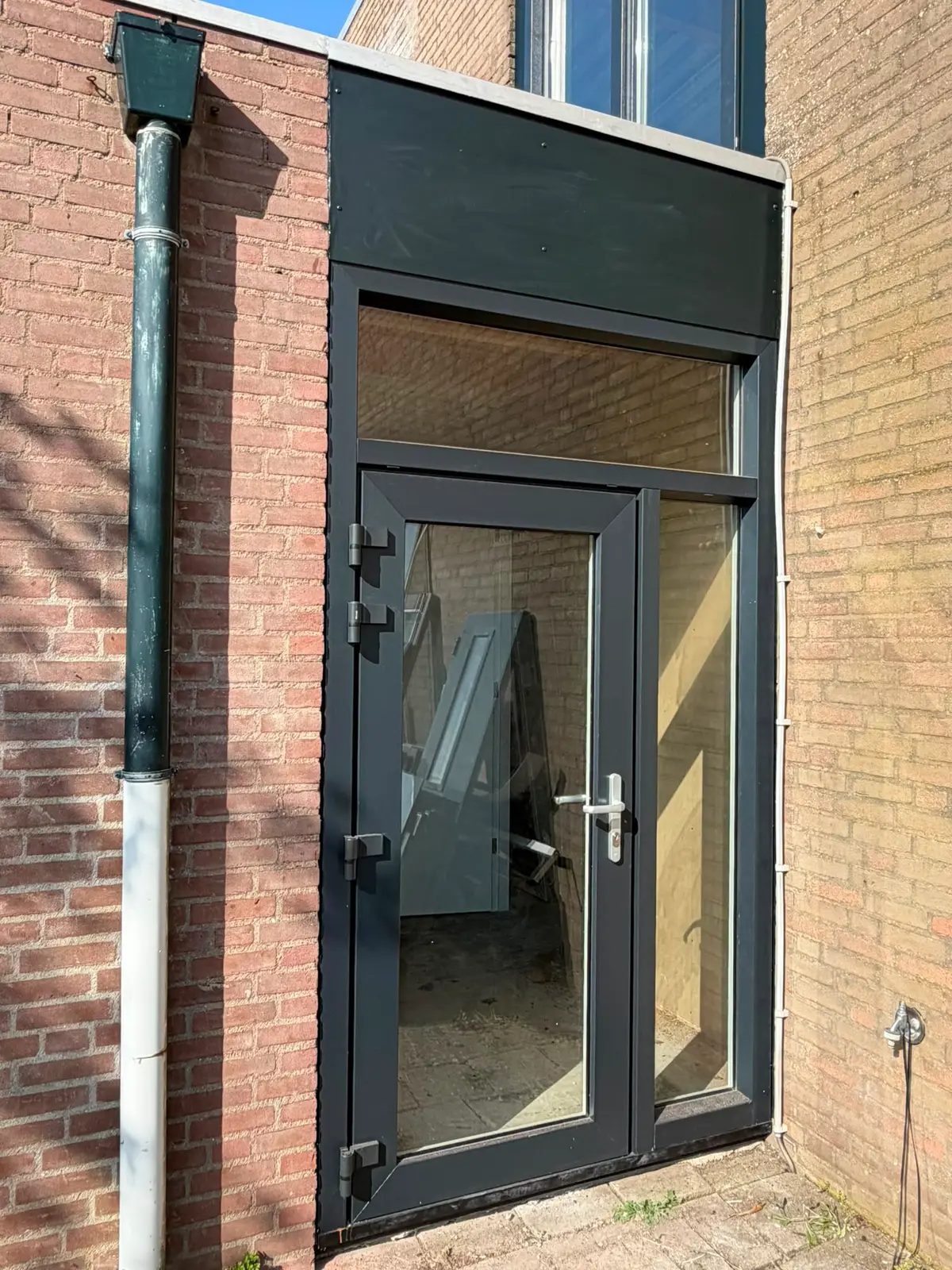 Antraciete kunststof deur met zijlicht in een bakstenen gevel